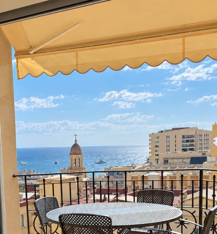 The covered terrace under its yellow awning, looking over rooftops and a church dome to the blue sea